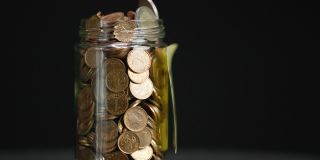 旋转玻璃罐装满硬币和两欧元硬币与粘贴的加密投资文本黑色背景，慢动作