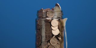装有硬币和两枚欧元硬币的旋转玻璃罐，上面粘贴有加密货币投资文字，蓝色背景，慢动作