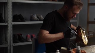 专业鞋匠在黑色胶乳喷涂浅棕色皮鞋的跟踪拍摄。视频素材模板下载