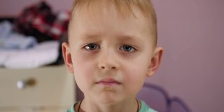 一个金发碧眼的愤怒男孩的肖像站在房间的摄像机前。