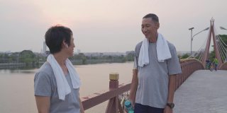 快乐的老年夫妇提供瓶装水后，在傍晚日落锻炼。微笑甜蜜的亚洲老年情人浪漫分享美好的时刻在一起。成熟的运动服装在桥公园休息。