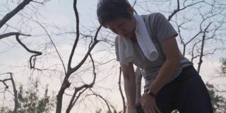 年长的亚洲活跃妇女膝盖受伤事故，在树木公园在日落。成熟女性用手按摩腿部以减轻疼痛。肌腱和肌肉问题。关闭轮廓。老年人的健康