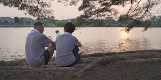 快乐的老夫妇坐在湖景附近提供瓶装水在傍晚日落。微笑甜蜜的亚洲老年情人浪漫分享美好的时刻在一起。运动成熟于运动服休憩于公园。