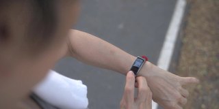一名亚洲老年妇女在公园的树下触摸智能手表活动跟踪器。手指敲击运动手表卡路里和心率信息。慢动作轨道拍摄。医疗保健俯视图。