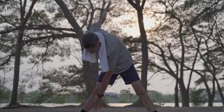 快乐的老人锻炼和伸展在湖边公园的树下在傍晚日落。亚洲老年男性户外活动锻炼。健身锻炼成熟。轮廓。老人保健理念。