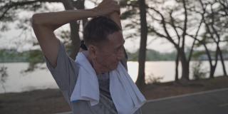 快乐的老人锻炼和伸展在湖边公园的树下在傍晚日落。亚洲老年男性户外活动锻炼。健身锻炼成熟。轮廓。老人保健理念。