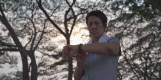 一名亚洲老年妇女在公园的树下触摸智能手表活动跟踪器。手指敲击运动手表卡路里和心率信息。慢动作轨道拍摄。卫生保健的概念。