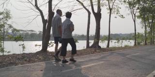 快乐的老夫妇手牵着手在傍晚日落公园散步锻炼。笑脸活跃的亚洲老年情人一起户外活动分享美好时刻。健身二人在公园成熟锻炼。