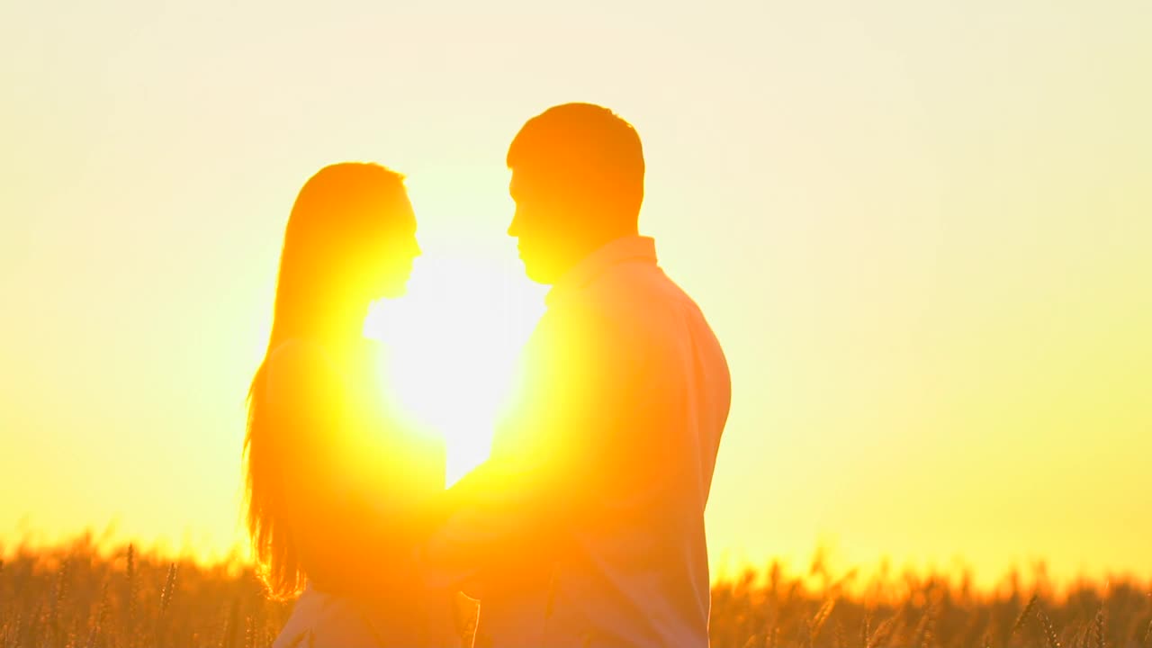 浪漫的年轻幸福的夫妇剪影在金色的麦田日落。女人和男人在阳光下拥抱亲吻，太阳镜头的光晕。爱，幸福的家庭，自然，户外。慢镜头,120 fps