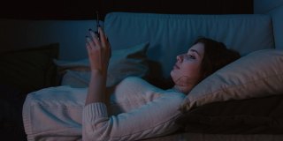 千禧一代女性躺在床上拿着手机，在在线约会应用上刷照片，在社交网络上输入信息。智能手机成瘾