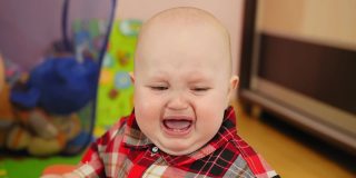 9个月大的婴儿穿着格子衬衫在家里哭闹。