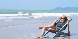 4K年轻的亚洲男子在海边的沙滩椅上休息。