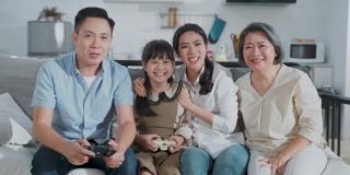 亚洲父亲和女儿与家人一起在家里的客厅玩主机游戏。妈妈和奶奶坐在他们旁边欢呼爸爸和孩子感到兴奋和有趣的笑容