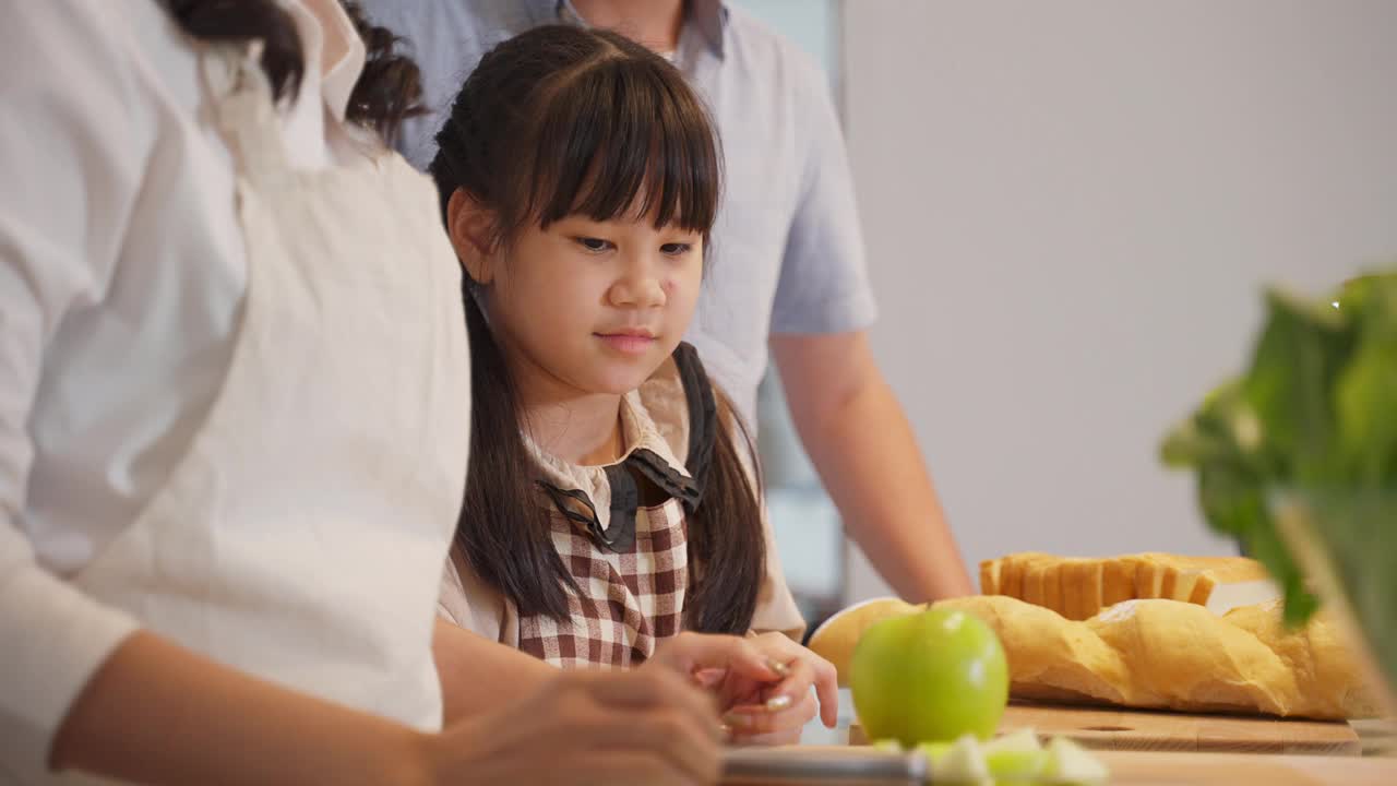 家庭关系，亚洲幸福家庭在厨房准备食物。父亲，母亲和孩子一起玩的时间。爸爸和小女孩看着妈妈做饭。