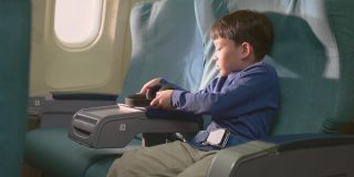 亚洲小男孩在飞机上触摸屏幕，然后看电影和卡通。孩子们感到高兴和兴奋的飞机旅行和享受机上娱乐。