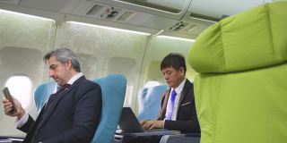 一群坐在飞机上用笔记本电脑或手机工作的商务舱乘客。乘务员走上前通知乘客关闭电子设备，以确保机上机组人员的安全。