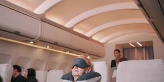亚洲空乘人员在飞机上为老年乘客盖毯子，商务舱，飞机概念。4 k UHD片段。