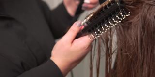一个理发师用吹风机、圆发刷吹干头发的特写。