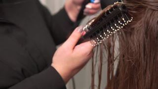 一个理发师用吹风机、圆发刷吹干头发的特写。视频素材模板下载