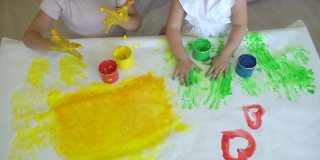 幸福家庭油漆颜色。近距离的快乐的小可爱的孩子的手在纸上画彩色的图画。一个可爱快乐有趣的小女孩画颜色，慢镜头