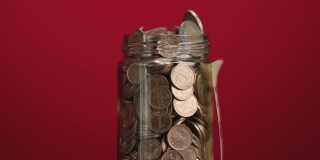 旋转玻璃罐装满硬币和两欧元硬币与粘贴的加密投资文字红色背景，慢动作
