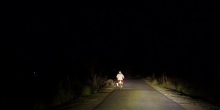 在柏油路上开车的4k视频。在柏油路上，司机超过一个骑自行车的人和一辆车的前灯。道路上的大灯光束具有极强的聚焦光。