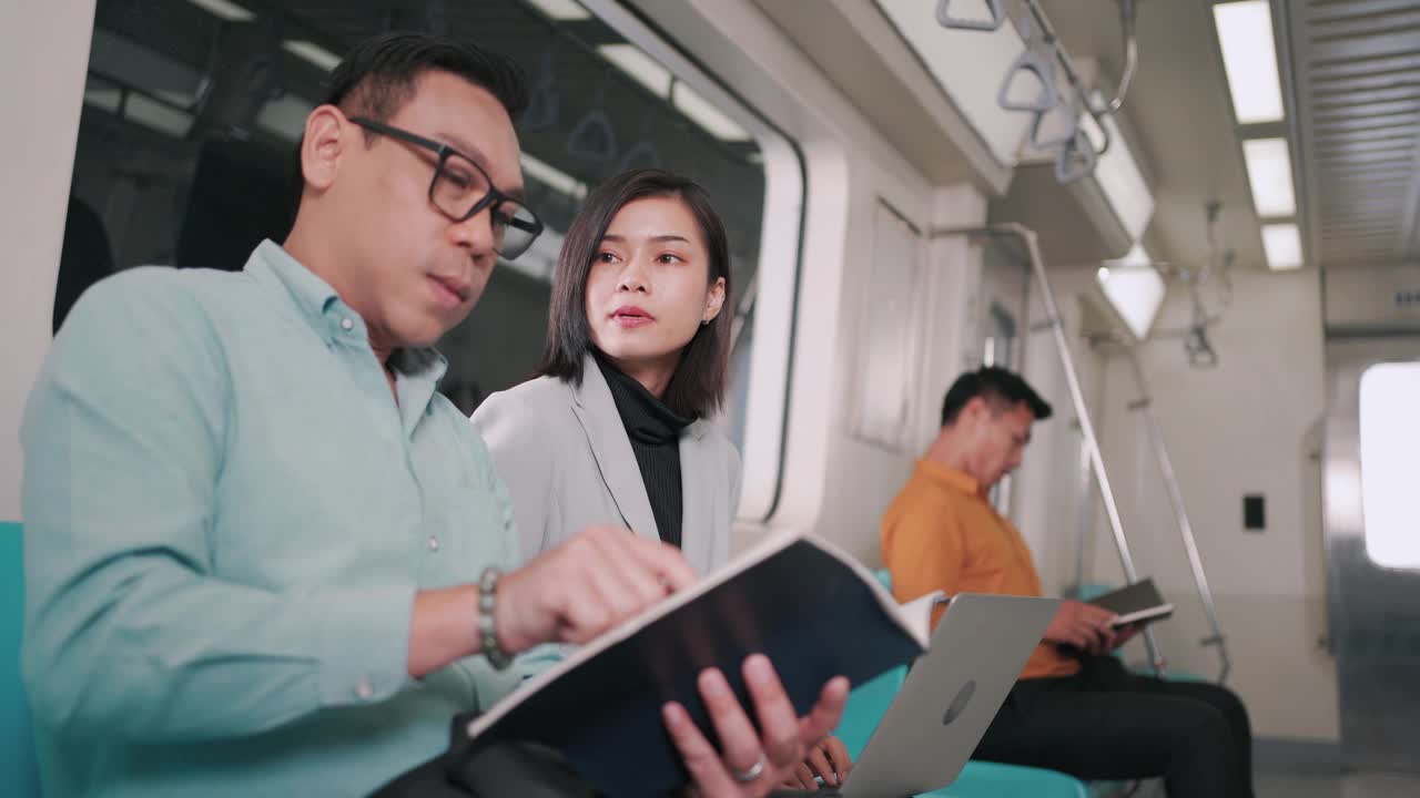商人在空中火车或地铁上使用笔记本电脑与女商人交谈，他们的工作交通工具，人们的生活理念。