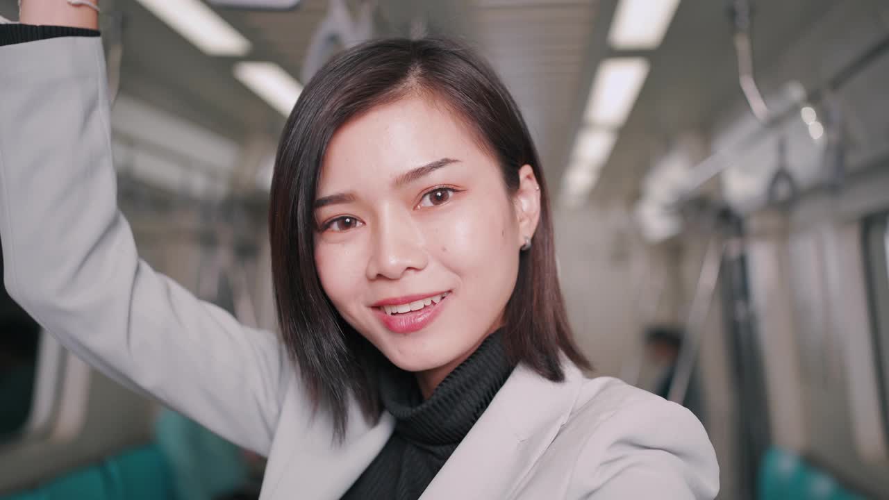 美丽的Asain女商人自拍，视频博客与手机在空中列车或地铁使用智能手机他们的方式工作运输人们的生活方式和无线连接的概念。