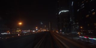 迪拜地铁在夜间驶过市中心的摩天大楼。地铁列车在地铁轨道上快速行驶的第一人称视角