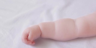 靠近可爱的小裸手可爱的蹒跚学步的婴儿躺在柔软的白色床上俯视图