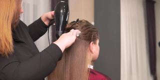 一位美发师在美容院为一位女士用吹风机吹干头发。