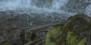 潮湿的石头在山瀑布的背景。水柱形成泡沫飞溅而下。透过清澈的溪流可以看到石底。河崖青苔