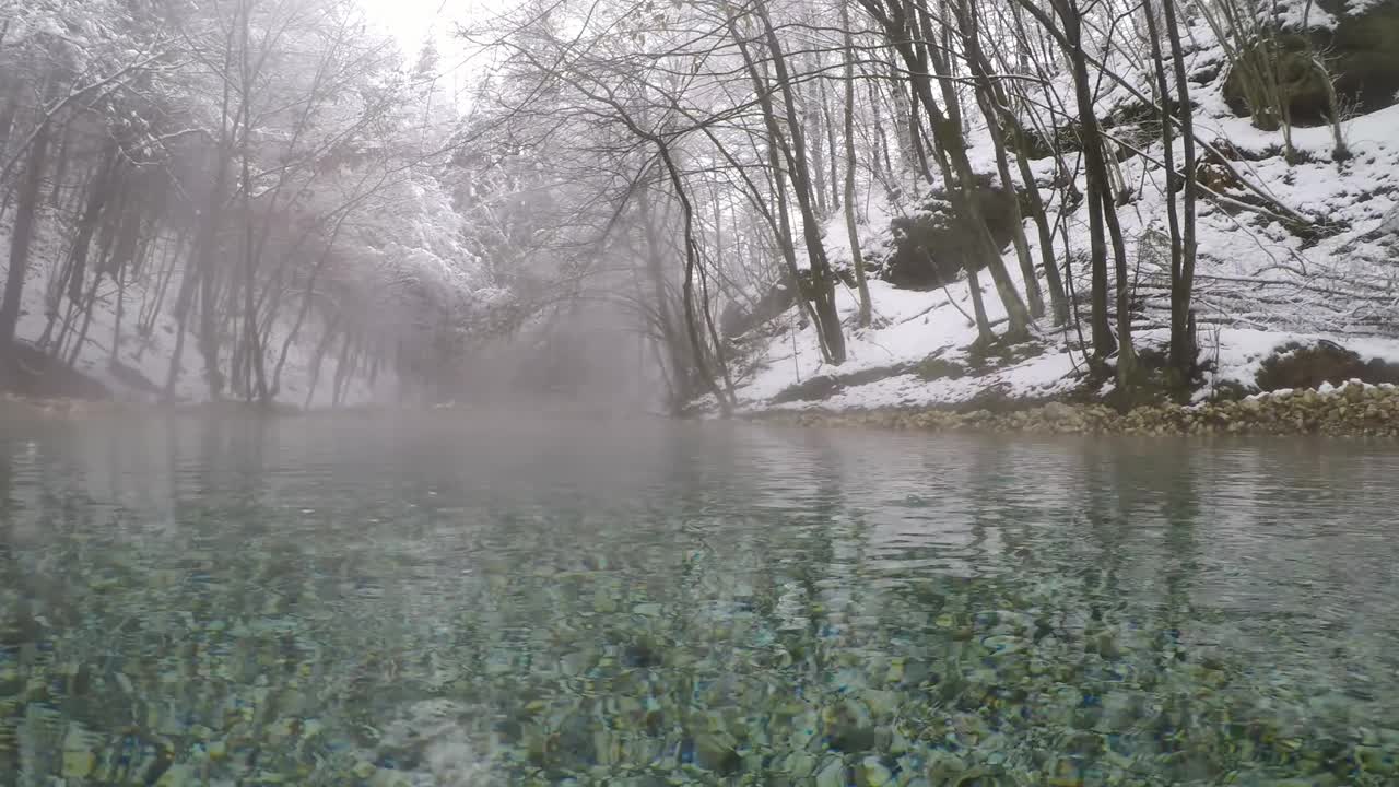 奥地利卡林西亚的一个温泉池。湖被雪包围着。周围还有一片茂密的森林。泡沫在池塘上冒着蒸汽。水滴在水面上摆动。自然能源。冬季室外