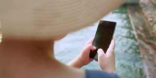 亚洲女性旅行者穿着休闲服装，享受假期日落时刻手用智能手机设备社交媒体交流。亚洲女性享受周末旅游游泳池日落时间。