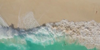 鸟瞰碧绿的海浪拍打着泡沫在光滑的沙滩上