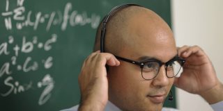年轻的亚洲教师男子教授视频会议与学生。男性印度教师在课堂上通过在线课程培训数学。他戴着一副小小的谈话耳机。