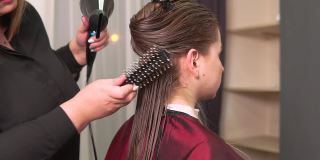 一名美发师用吹风机为一名年轻女子吹干长长的直发