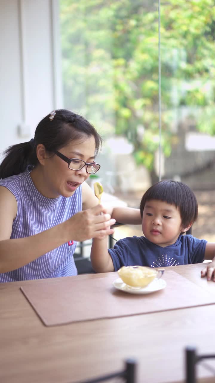 一个亚洲男婴和母亲在餐厅吃甜点的垂直镜头