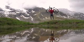 慢动作:山地车手把他的自行车举到空中。成就的概念。在山间小路上，一个人把他的自行车举到空中