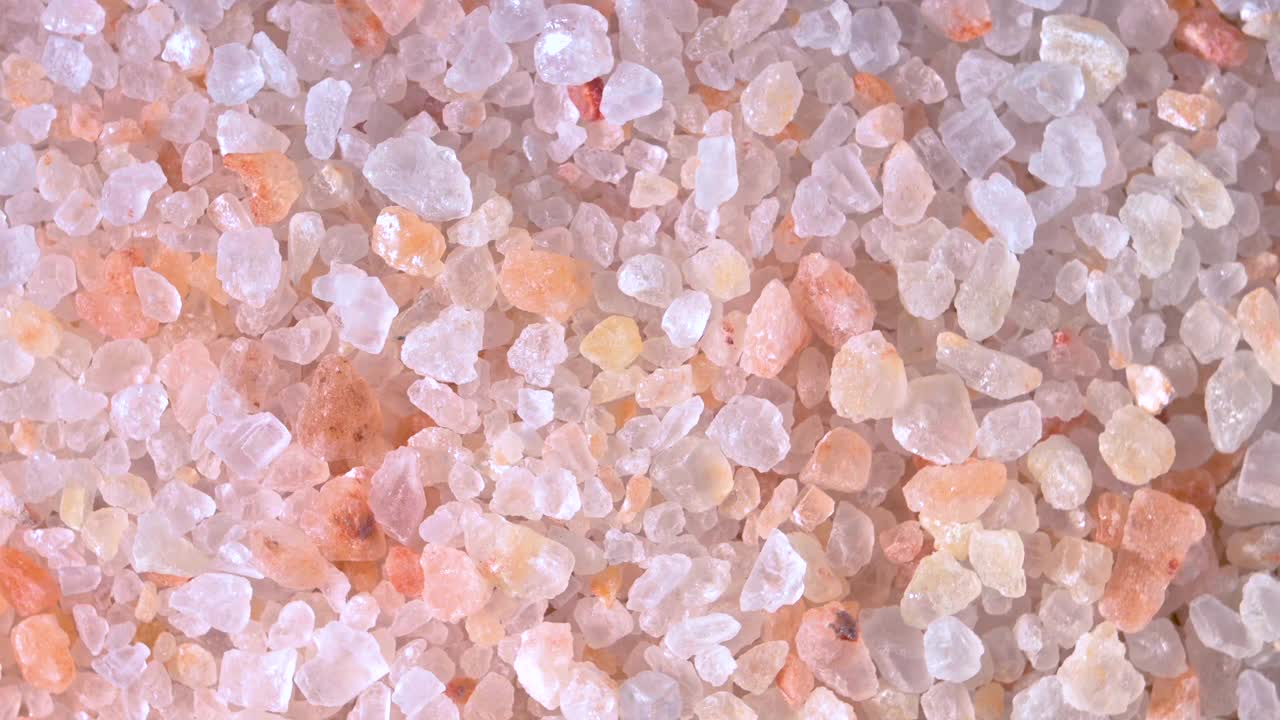 粉红色喜马拉雅盐。特写喜马拉雅粉岩盐在木勺黑色的背景。粉喜马拉雅盐的细粒