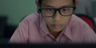 肖像可爱的亚洲年轻女孩戴着耳机从笔记本学习在线课程。严重的女性青少年通过家庭使用电脑上网。