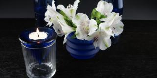 插花:一束白色的花，蓝色的玻璃花瓶和燃烧的蜡烛