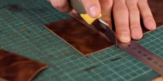 皮革匠的手的近距离测量和切割皮革与刀。生产手工皮具。爱好的概念。缓慢的运动。