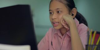 可爱的小女孩戴着耳机通过电脑摄像头在家向远程老师解释她的家庭作业。远程教育。