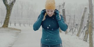 一名女子在雪地里慢跑前，将耳塞式耳机戴在耳朵上