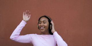 快乐的年轻拉丁女人用无线耳机跳舞听音乐