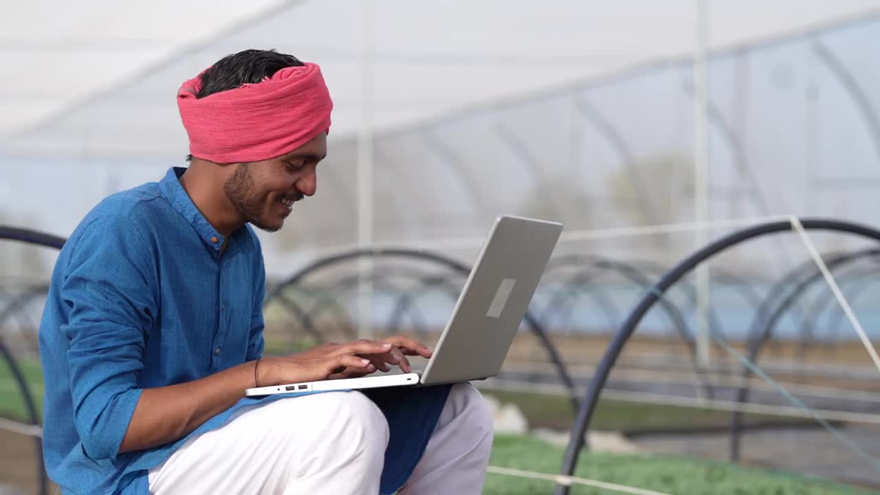年轻的印度农民在温室或poly房子里使用笔记本电脑