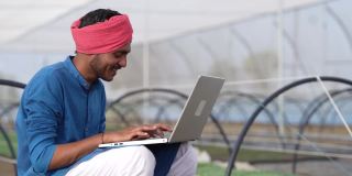 年轻的印度农民在温室或poly房子里使用笔记本电脑