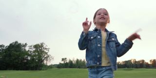 可爱的小女孩站在绿色的田野里玩肥皂泡，孩子们在户外的自然中度过休闲时光