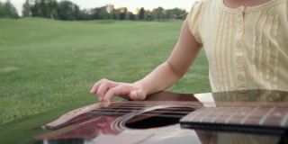 在温暖的夏日，小女孩坐在绿色的草地上弹着吉他，和家人一起在户外享受周末